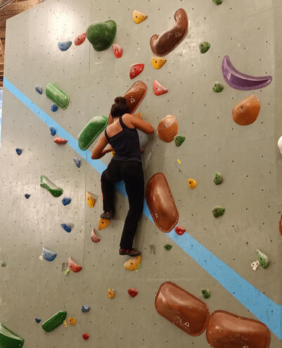 Click here for Sweet Earth Goa Guide Equilibrium Climbing Station in Anjuna, Goa. Covered rock climbing wall with climber ascending colorful holds.